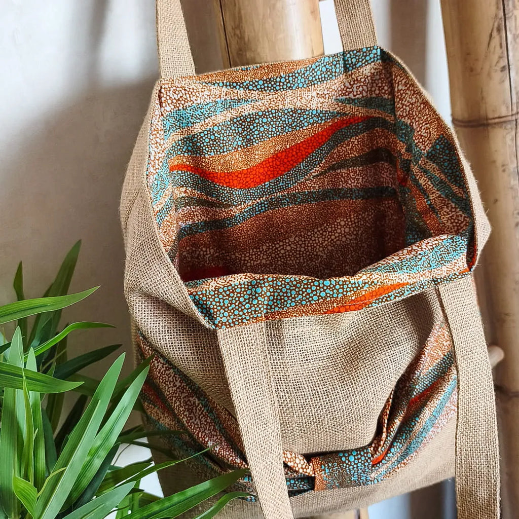 Sac cabas en toile de jute avec un gros nœud en tissu wax orange bleu et beige sur le devant et intérieur tout en wax
