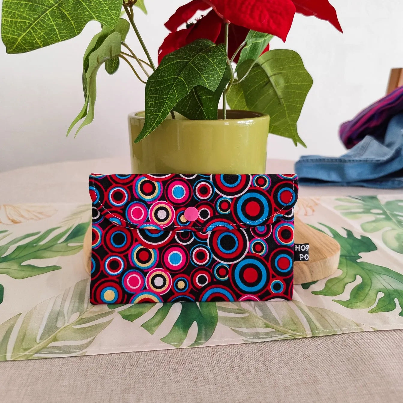 mini pochette format enveloppe en tissu wax motif cercles bleu rose et rouge sur une table