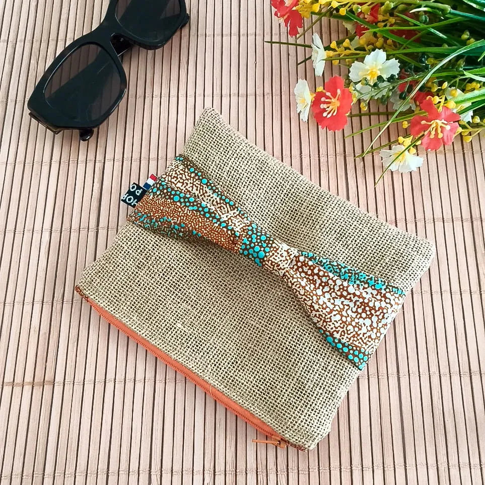 Pochette plate en toile de jute avec un nœud en tissu Wax orange bleu et beige sur le devant