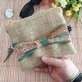 Pochette plate en toile de jute avec un nœud en tissu Wax orange bleu et beige sur le devant tenu dans une main