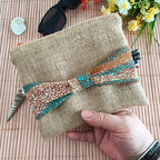 Pochette plate en toile de jute avec un nœud en tissu Wax orange bleu et beige sur le devant tenu dans une main