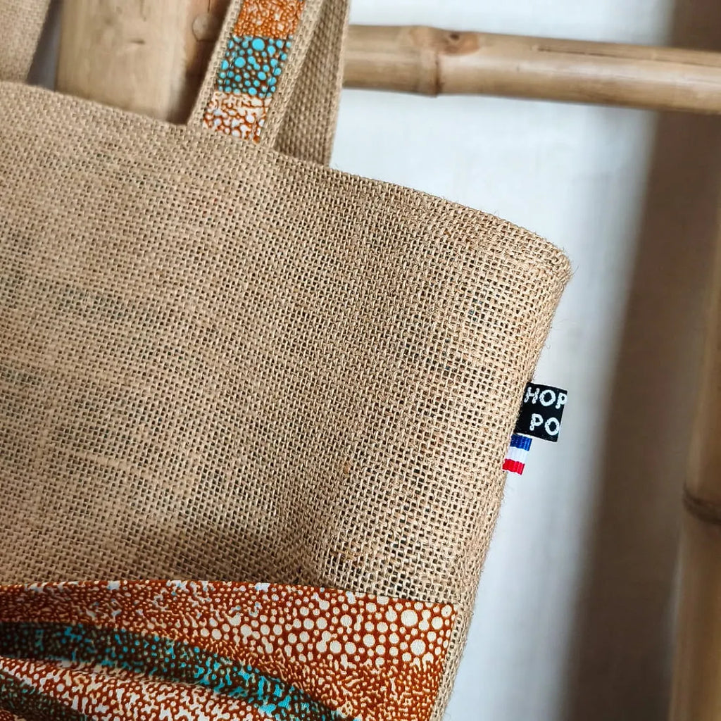 Sac cabas en toile de jute avec un gros nœud en tissu wax orange bleu et beige sur le devant vue du haut du sac