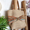 Sac cabas en toile de jute avec un gros nœud en tissu wax orange bleu et beige sur le devant